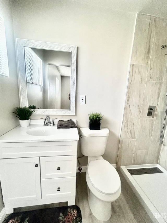 full bathroom with a tile shower, toilet, vanity, and baseboards