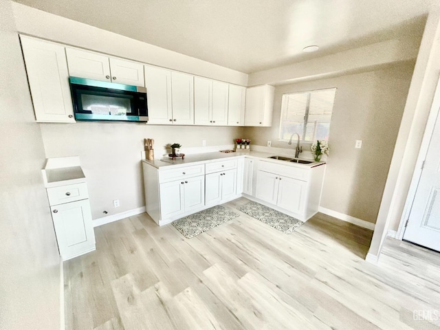 kitchen featuring white cabinetry, stainless steel microwave, light wood finished floors, and a sink