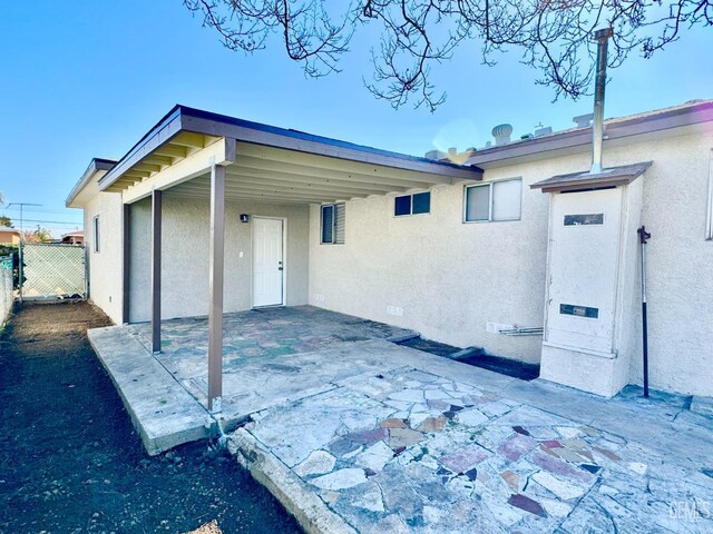 rear view of property with stucco siding, a carport, a patio area, and fence