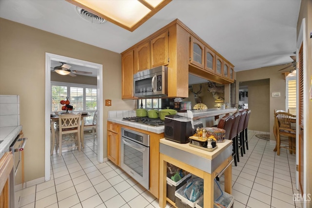 kitchen with tile countertops, ceiling fan, light tile patterned flooring, and appliances with stainless steel finishes