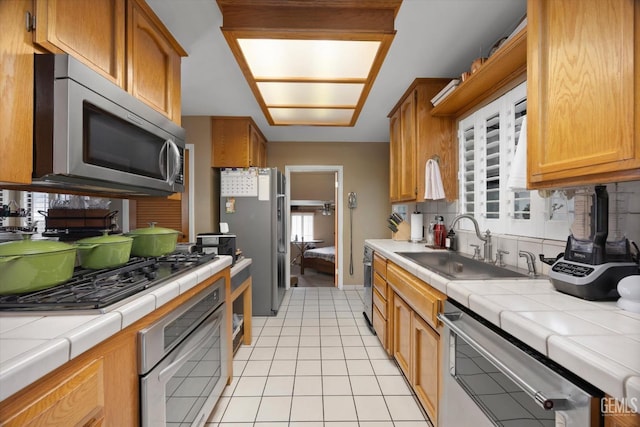 kitchen featuring tile counters, sink, light tile patterned floors, and stainless steel appliances