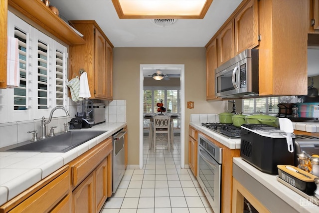 kitchen with appliances with stainless steel finishes, tasteful backsplash, sink, tile counters, and light tile patterned flooring