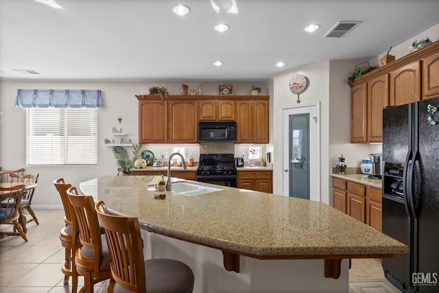 kitchen with black appliances, a kitchen bar, a sink, visible vents, and a center island with sink