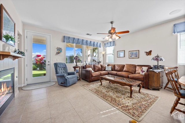 living room with visible vents, light tile patterned floors, a tile fireplace, and ceiling fan