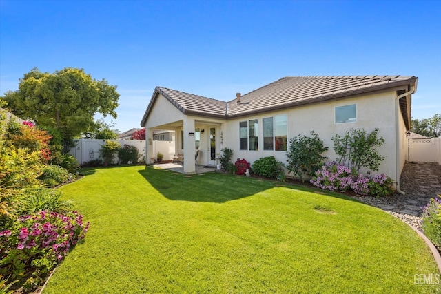 back of house featuring stucco siding, a yard, a tile roof, and a fenced backyard