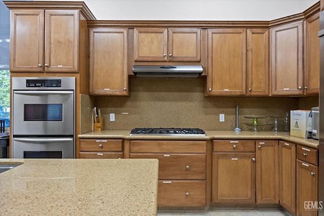 kitchen featuring under cabinet range hood, tasteful backsplash, appliances with stainless steel finishes, and brown cabinets