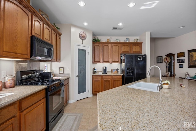 kitchen with brown cabinetry, light tile patterned floors, black appliances, a sink, and visible vents