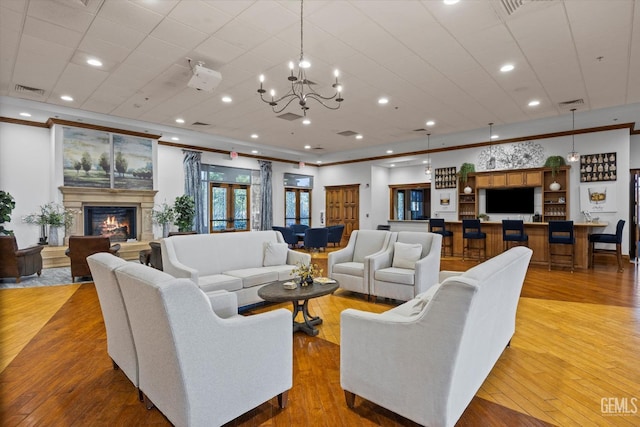 living room with crown molding, visible vents, an inviting chandelier, a glass covered fireplace, and light wood finished floors