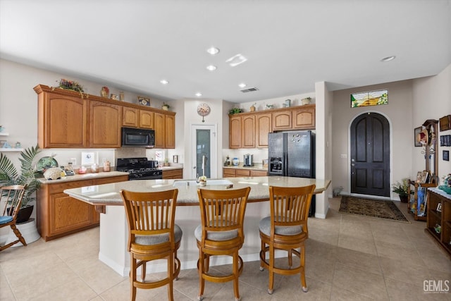 kitchen with black appliances, light tile patterned flooring, an island with sink, and a sink