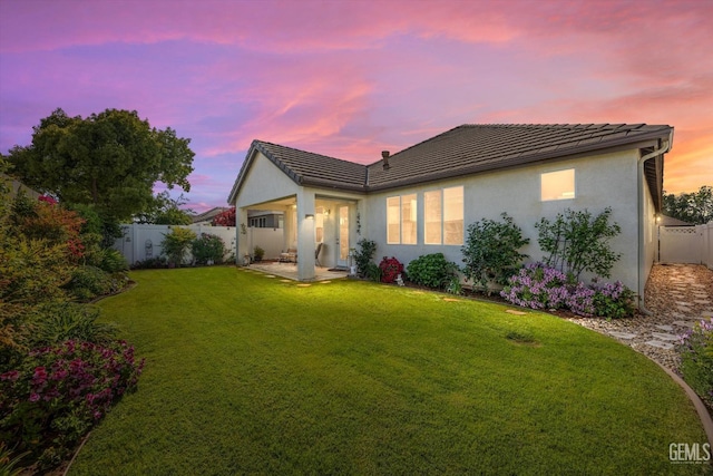 back of house at dusk featuring stucco siding, a tiled roof, a yard, and a fenced backyard