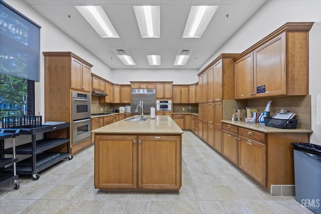 kitchen featuring appliances with stainless steel finishes, brown cabinets, a kitchen island with sink, and a sink