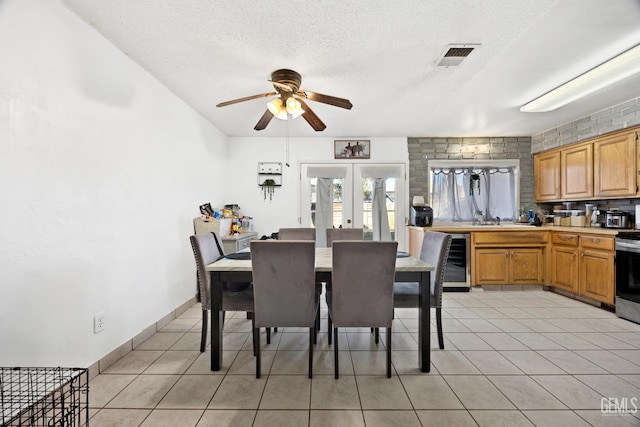 tiled dining area featuring french doors, sink, a textured ceiling, ceiling fan, and beverage cooler