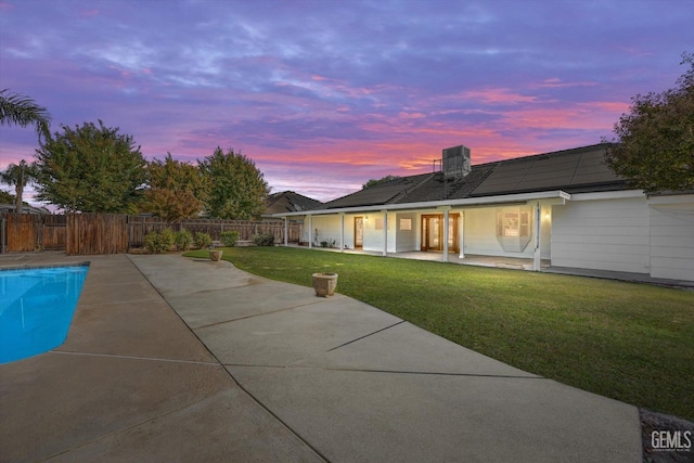 back house at dusk featuring a lawn, solar panels, a patio area, and a fenced in pool