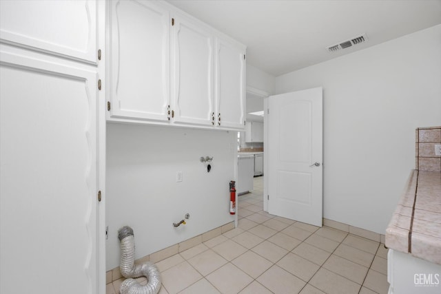 clothes washing area with hookup for a gas dryer, light tile patterned floors, and cabinets