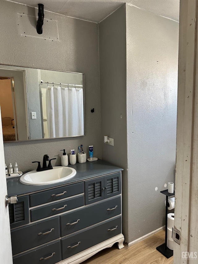 full bathroom featuring a textured wall, vanity, baseboards, and wood finished floors