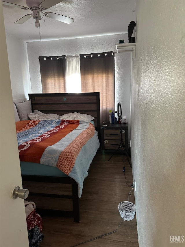 bedroom with dark wood-style floors, a textured wall, and a ceiling fan