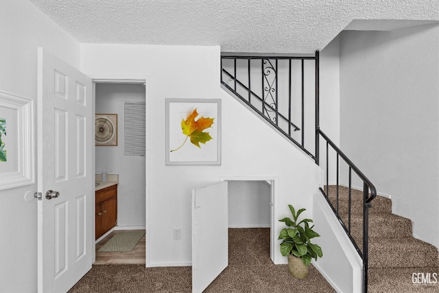 stairway with a textured ceiling, carpet, and baseboards