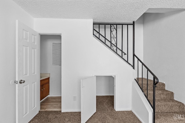 stairway with carpet, baseboards, and a textured ceiling