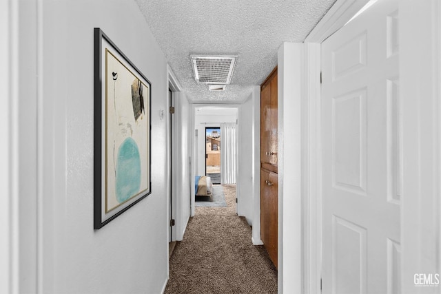 corridor featuring a textured ceiling, dark colored carpet, and visible vents