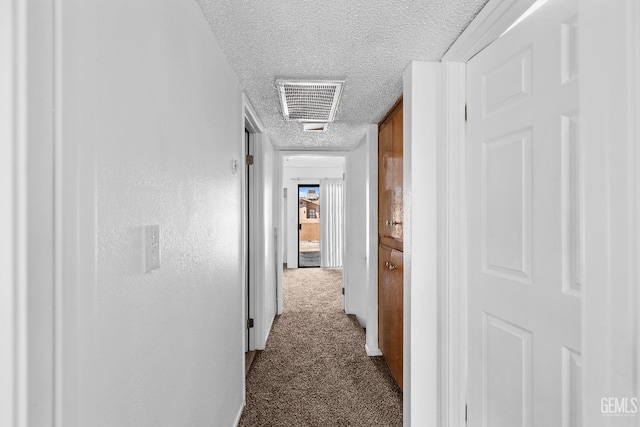 hall featuring visible vents, dark carpet, and a textured ceiling