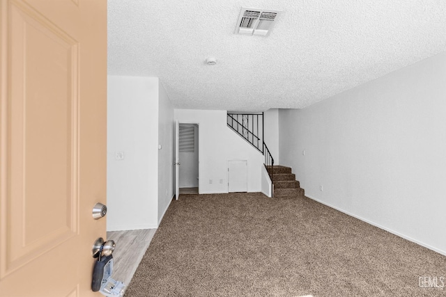 interior space featuring carpet floors, visible vents, a textured ceiling, and stairs