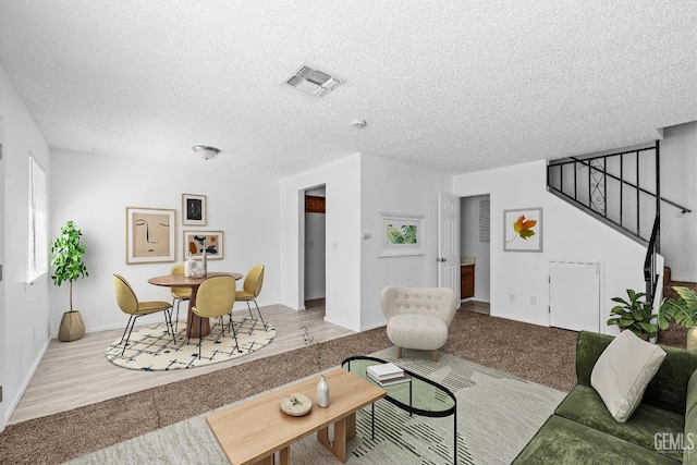 living room with a textured ceiling, stairway, wood finished floors, and visible vents