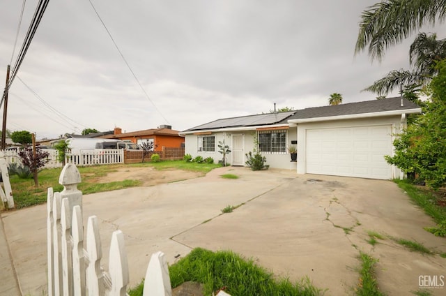 ranch-style home featuring solar panels, concrete driveway, fence, an attached garage, and stucco siding
