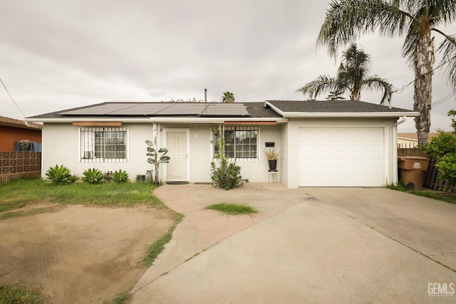 single story home with driveway, fence, an attached garage, roof mounted solar panels, and stucco siding