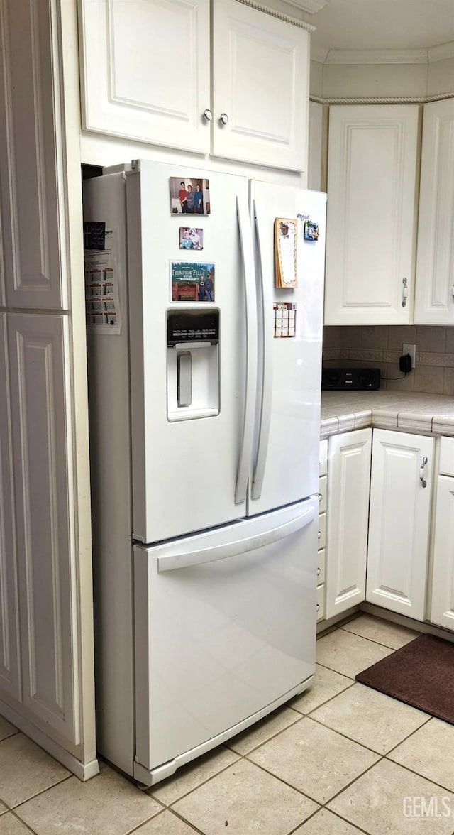 kitchen with white refrigerator with ice dispenser, tile counters, decorative backsplash, white cabinetry, and light tile patterned flooring