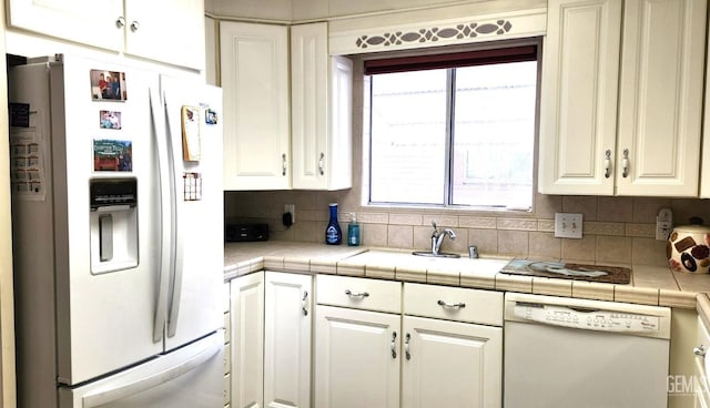 kitchen with tile counters, white appliances, a sink, and tasteful backsplash