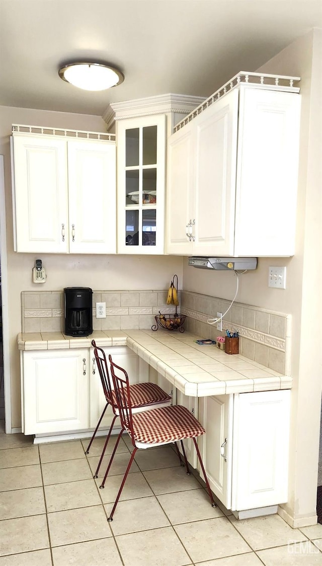 kitchen with glass insert cabinets, white cabinets, tile countertops, and light tile patterned flooring