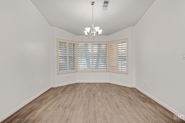 spare room featuring a chandelier, light wood-type flooring, visible vents, and baseboards