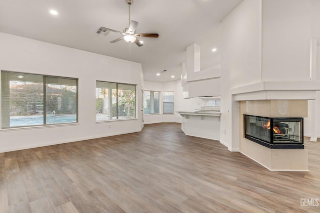 unfurnished living room featuring visible vents, light wood-style floors, a multi sided fireplace, ceiling fan, and baseboards