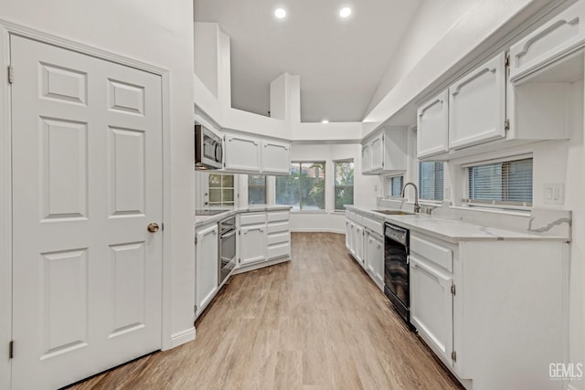 kitchen with light wood-style floors, light stone counters, black appliances, white cabinetry, and a sink