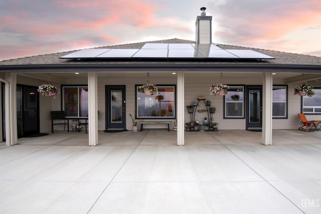 back of property at dusk with roof mounted solar panels, a shingled roof, and covered porch