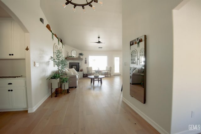 hall featuring light wood finished floors, arched walkways, and baseboards