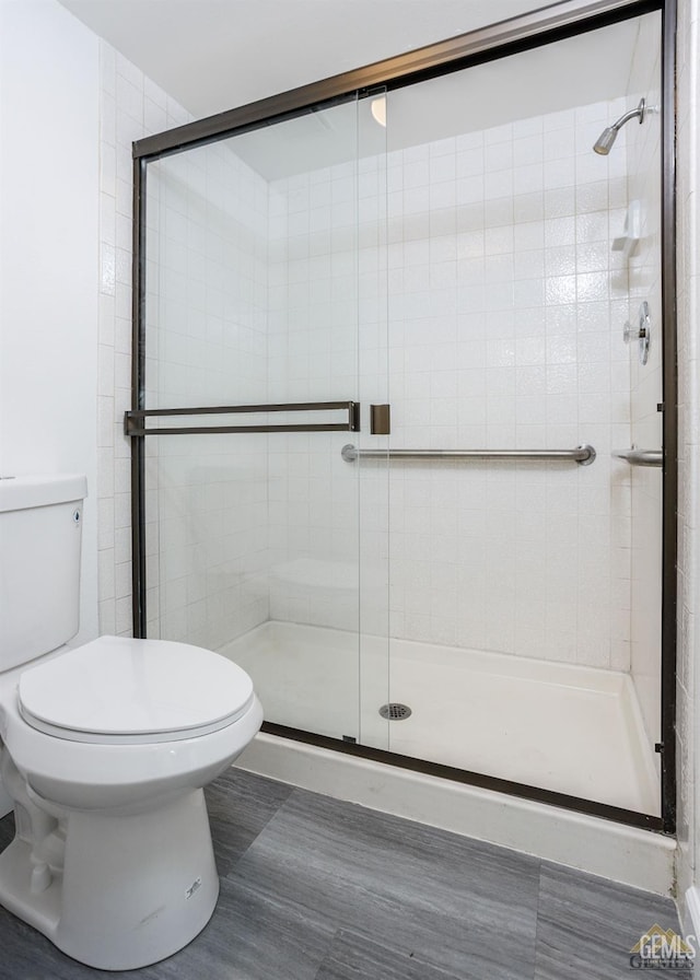 bathroom featuring a shower with door and toilet