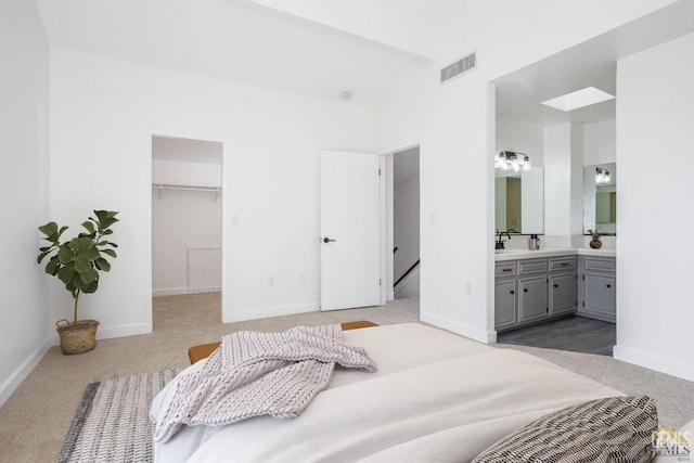 bedroom with a closet, a walk in closet, light carpet, and ensuite bath