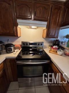 kitchen featuring light countertops, exhaust hood, dark brown cabinets, and electric range oven