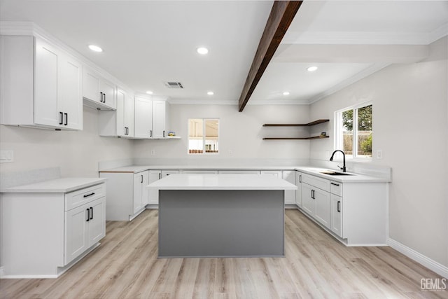 kitchen featuring open shelves, a sink, light wood finished floors, beamed ceiling, and visible vents