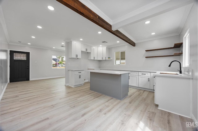 kitchen with open shelves, ornamental molding, a center island, a sink, and light wood finished floors