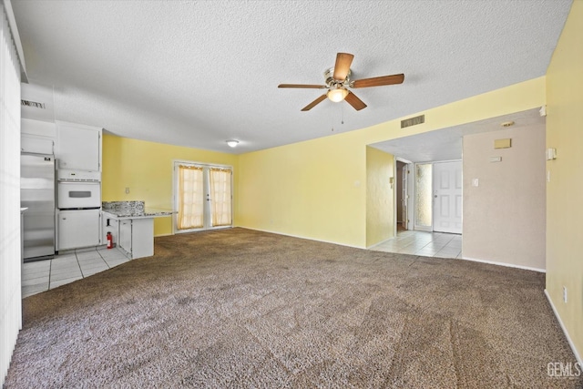 unfurnished living room featuring a textured ceiling, light tile patterned flooring, visible vents, and light carpet