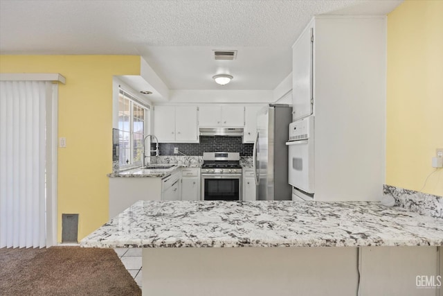 kitchen with visible vents, a peninsula, a sink, stainless steel appliances, and under cabinet range hood