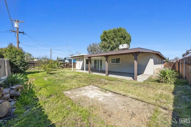 rear view of house with stucco siding, a lawn, a fenced backyard, and a patio area