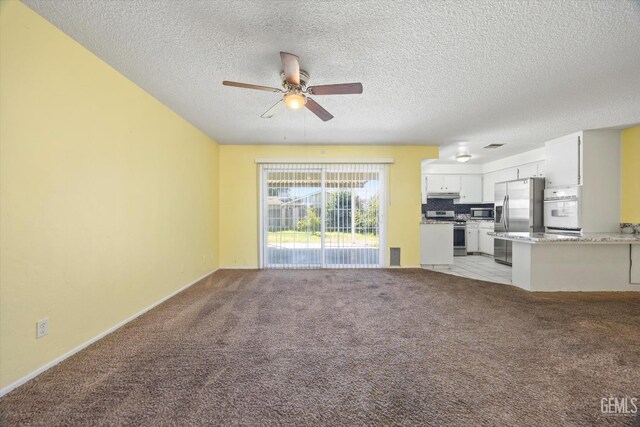 unfurnished living room featuring a ceiling fan, light colored carpet, and a textured ceiling