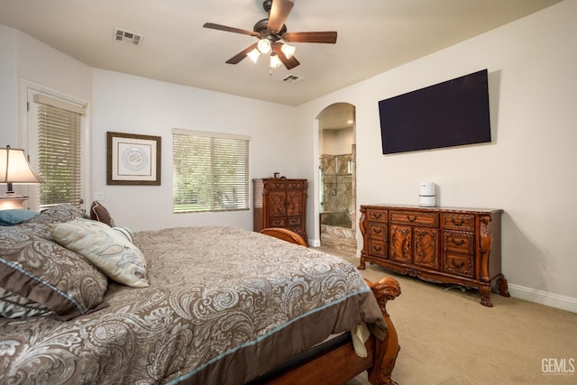 carpeted bedroom with arched walkways, visible vents, ensuite bath, and baseboards