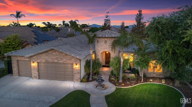 mediterranean / spanish house with a garage, driveway, stone siding, and a front yard