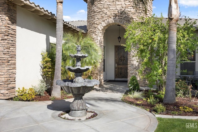 entrance to property with stucco siding, a tile roof, and stone siding