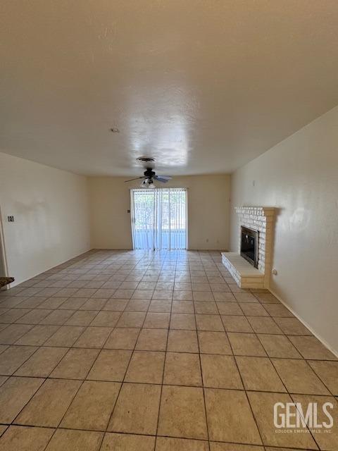 unfurnished living room with ceiling fan, light tile patterned flooring, and a fireplace