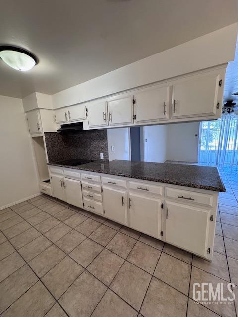 kitchen with light tile patterned flooring, white cabinetry, tasteful backsplash, dark stone countertops, and kitchen peninsula